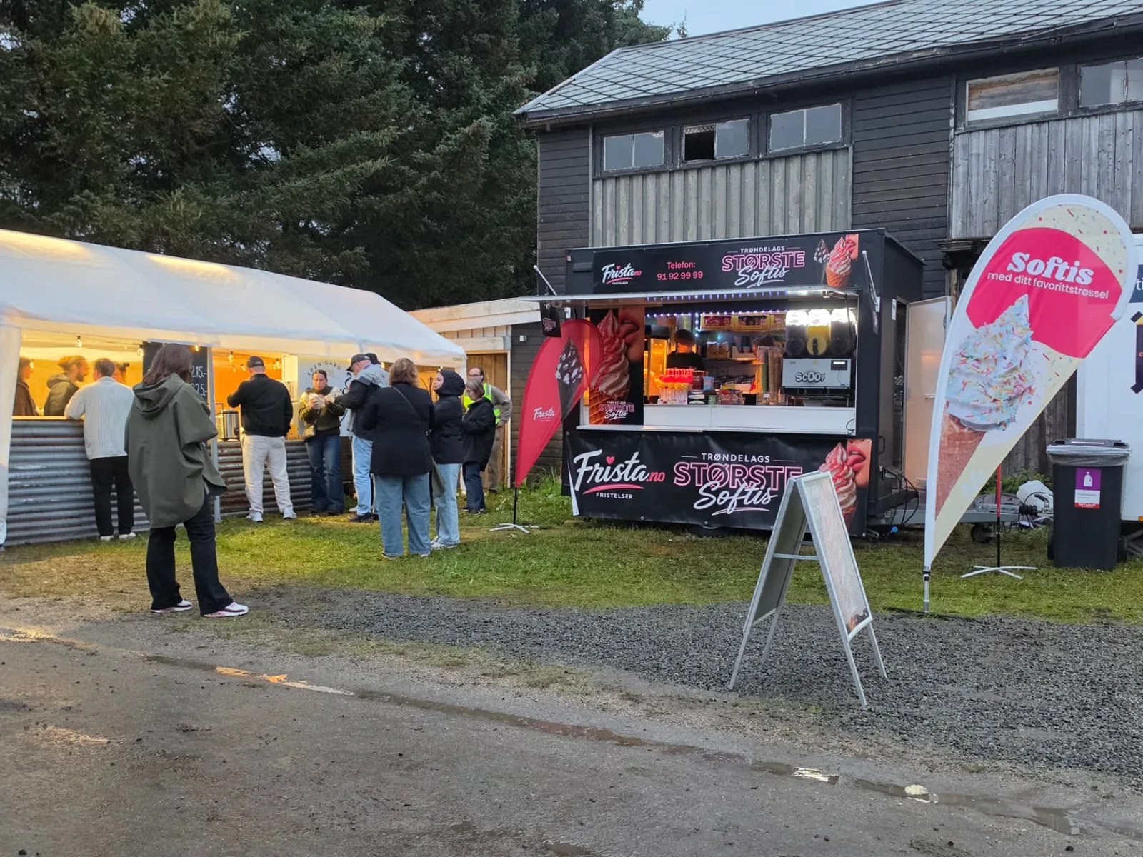 Frista Softis-vogna i kveldslys med kunder i kø ved siden av et serveringstelt